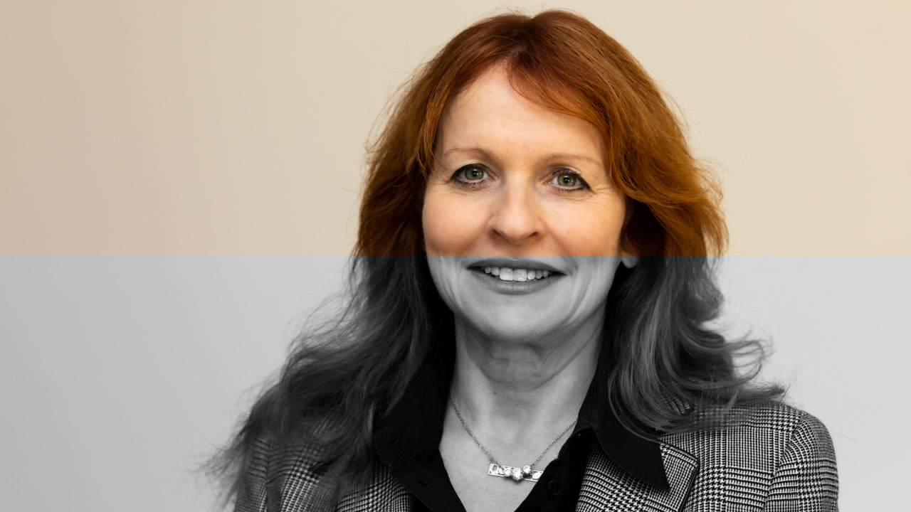 A professional portrait headshot of a woman with a split color and black-and-white effect, with the upper half in color and the lower half in black-and-white, set against a plain background.