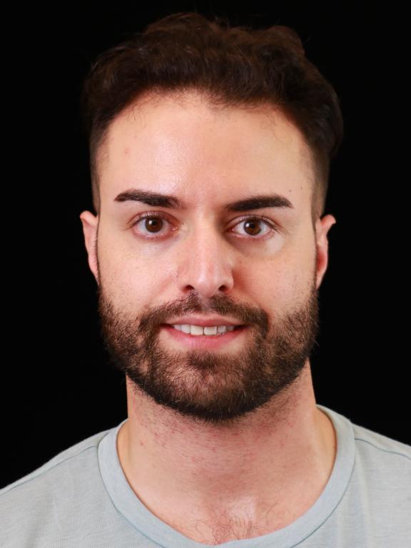 Portrait photograph of a man with a beard, wearing a light-colored shirt, against a black background.
