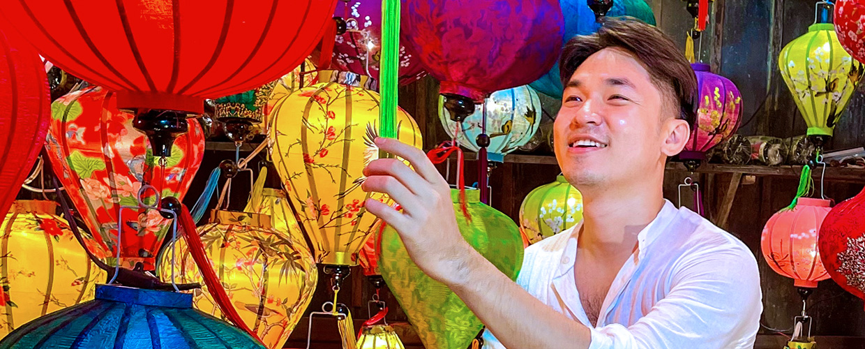 A smiling person in a white shirt surrounded by vibrant, colorful lanterns.