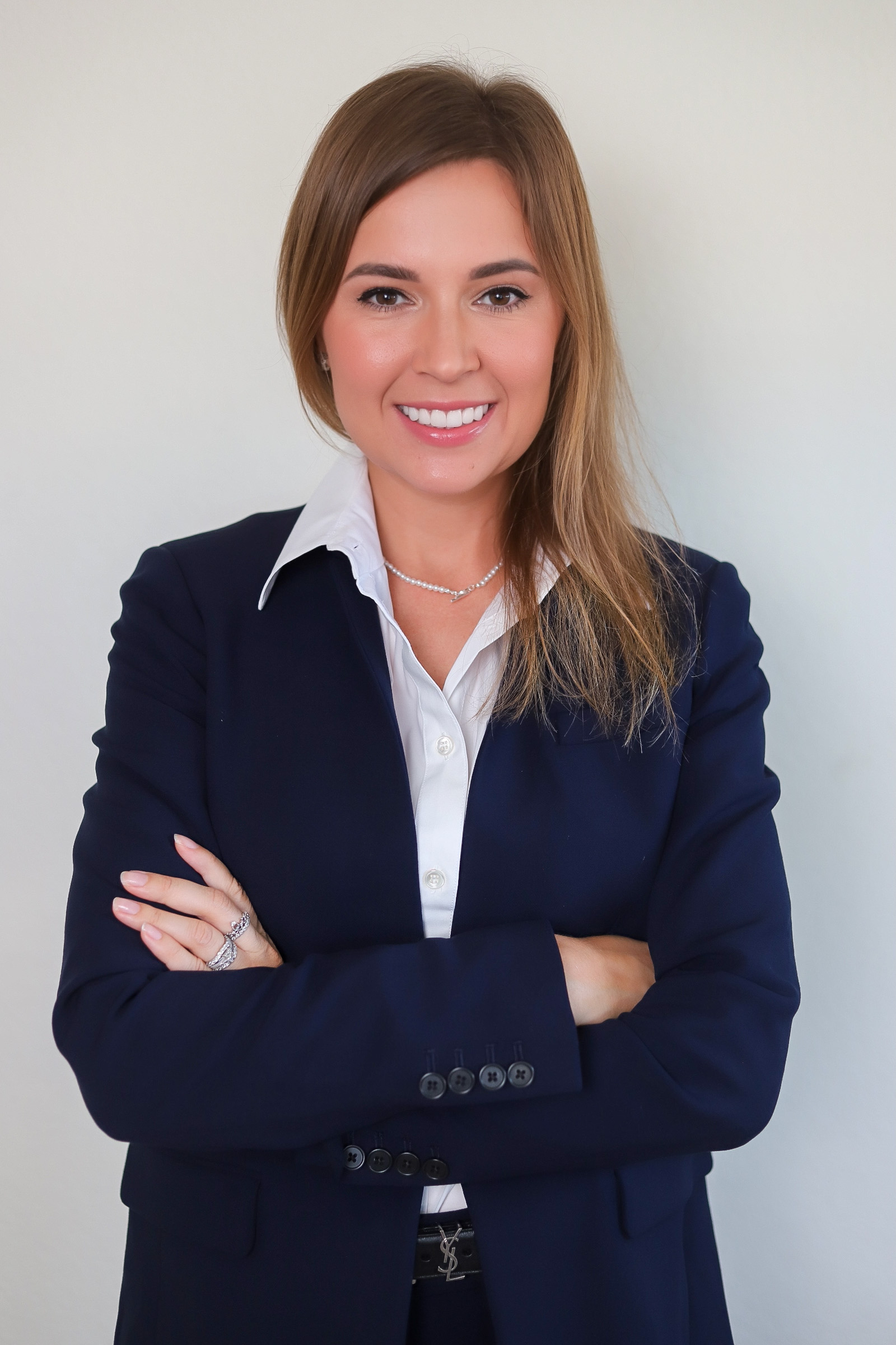Professional portrait of a businesswoman in a navy suit with arms crossed, smiling against a neutral background.