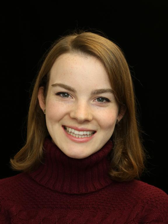 A portrait of a woman smiling, wearing a maroon sweater, with a black background.