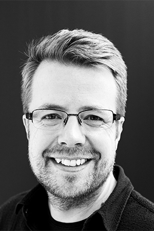 Black and white portrait of a smiling person wearing glasses