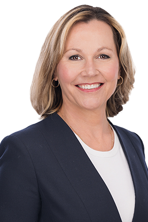 Professional portrait of a smiling blonde woman wearing business attire, photographed against a white background