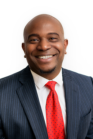 Professional portrait of Dr. Azizi Seixas, smiling and wearing a dark pinstripe suit with a red tie on a white background.