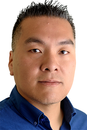Professional portrait headshot of a man with short dark hair wearing a blue collared shirt, facing forward against a white background.