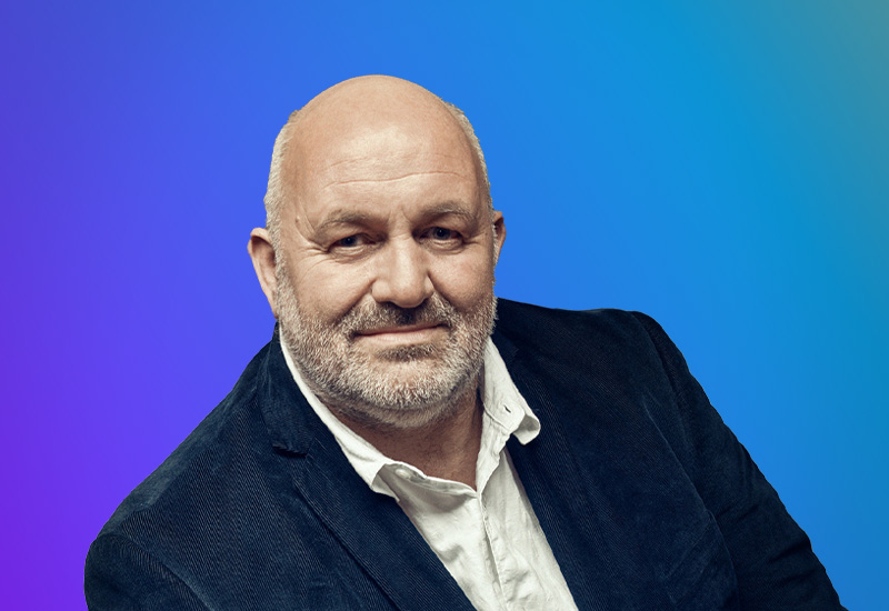 A person wearing a dark blazer and white shirt against a gradient blue and purple background.