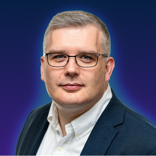 A person wearing a dark suit jacket and white collared shirt against a gradient blue background.