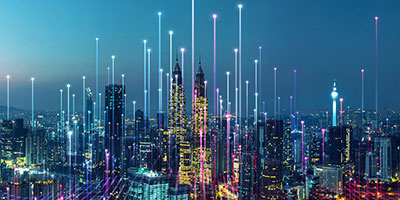 A city skyline at dusk illuminated with colorful digital light trails and glowing points, representing innovation and smart technology in urban environments.