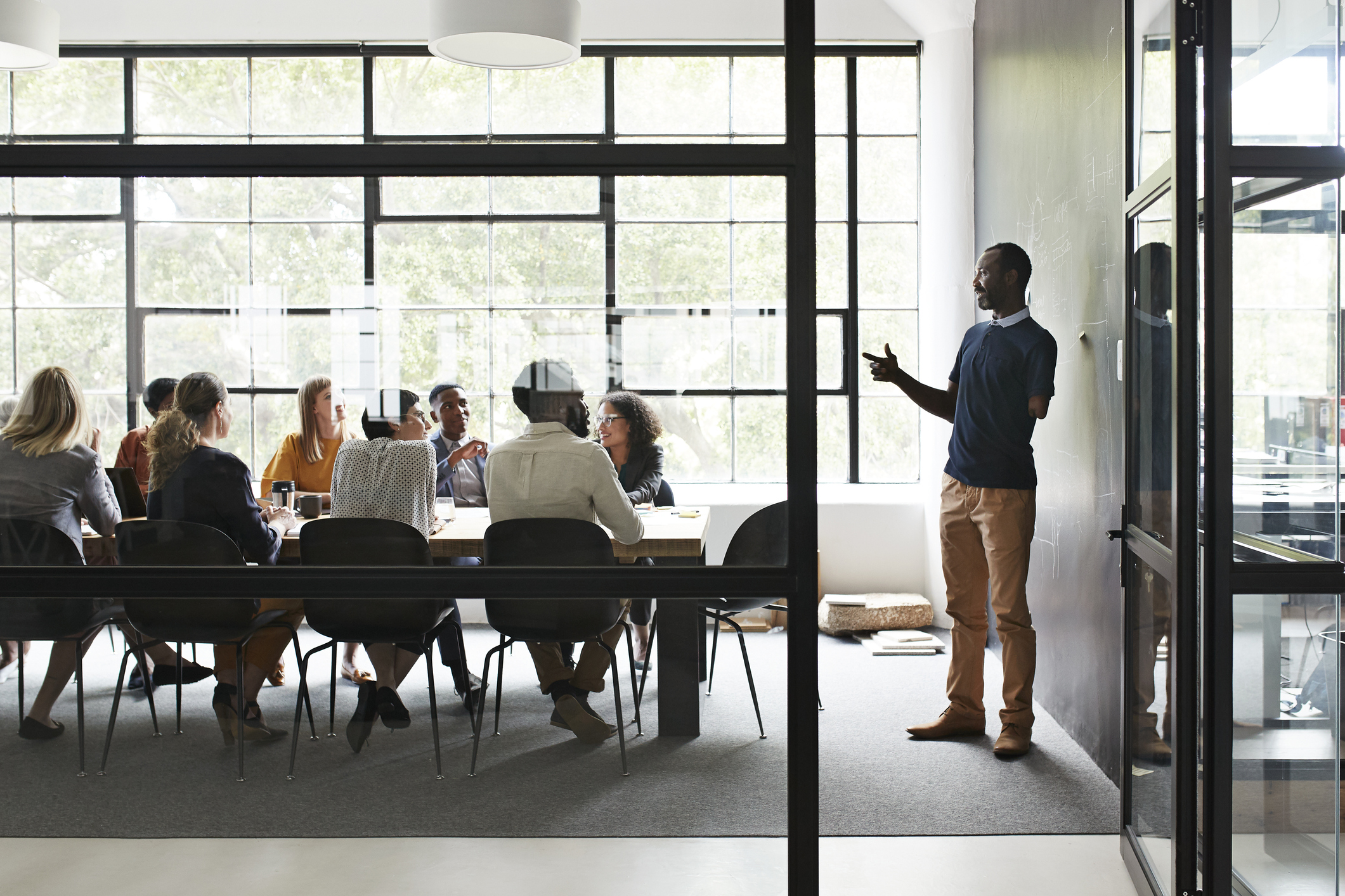 Amputated businessman explaining while female and male coworker sitting in board meeting at workplace seen through doorway