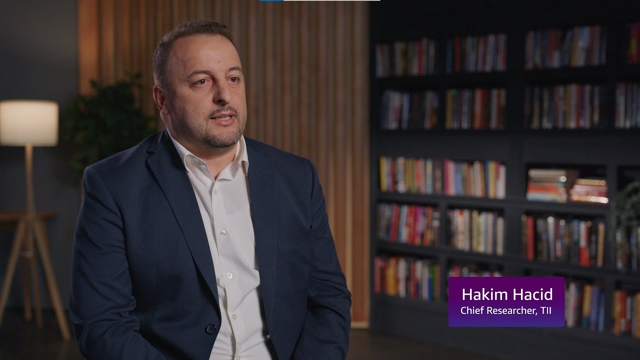 A man in a suit seated in a room with bookshelves and a lamp, with a label reading "Hakim Hacid, Chief Researcher, TII."