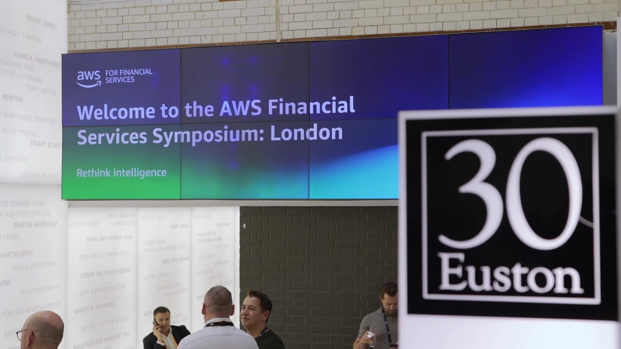 Signage reading "Welcome to the AWS Financial Services Symposium: London" with "30 Euston" displayed in the foreground.
