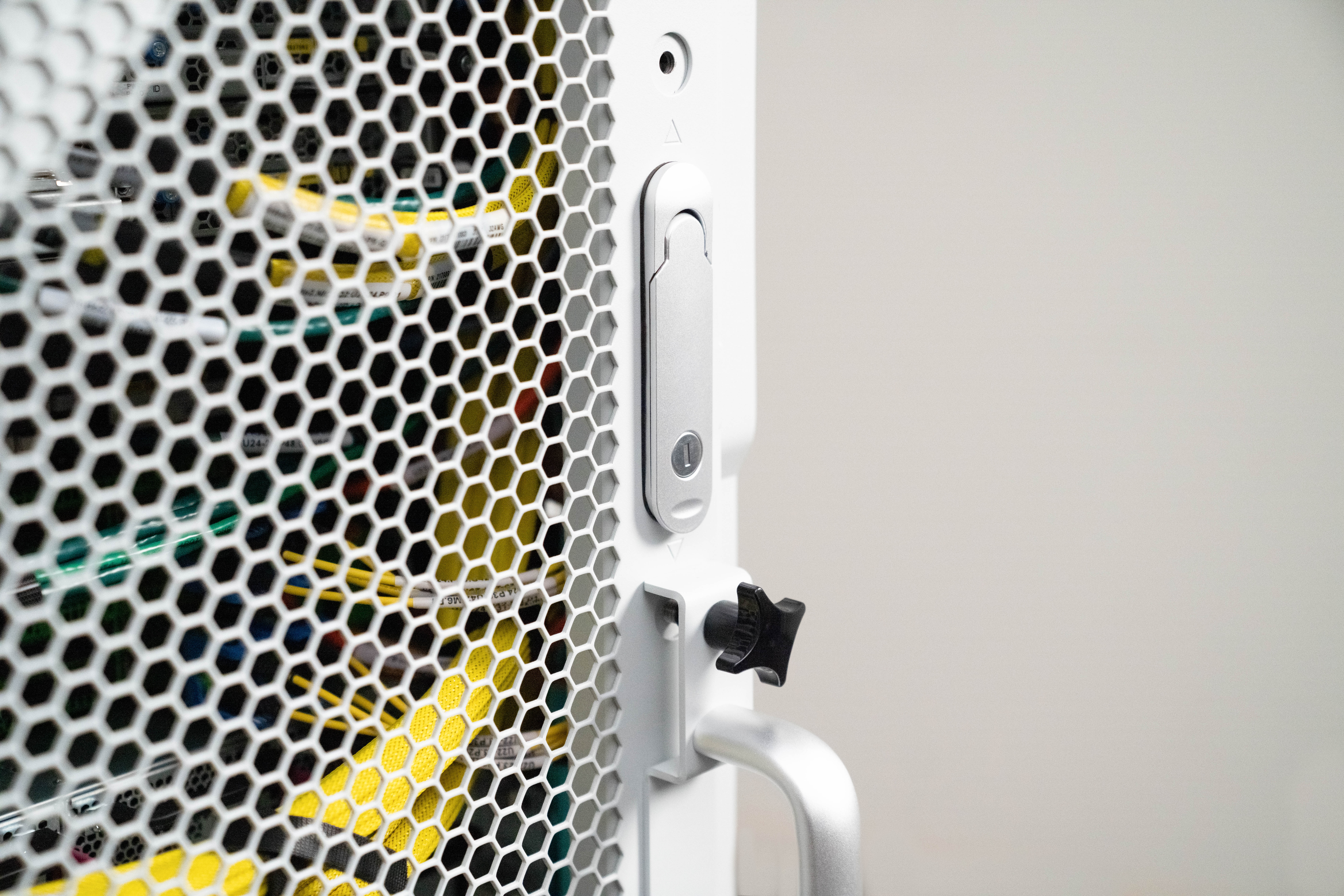 Close-up of a server rack with a hexagonal mesh door, showing colorful cables inside.