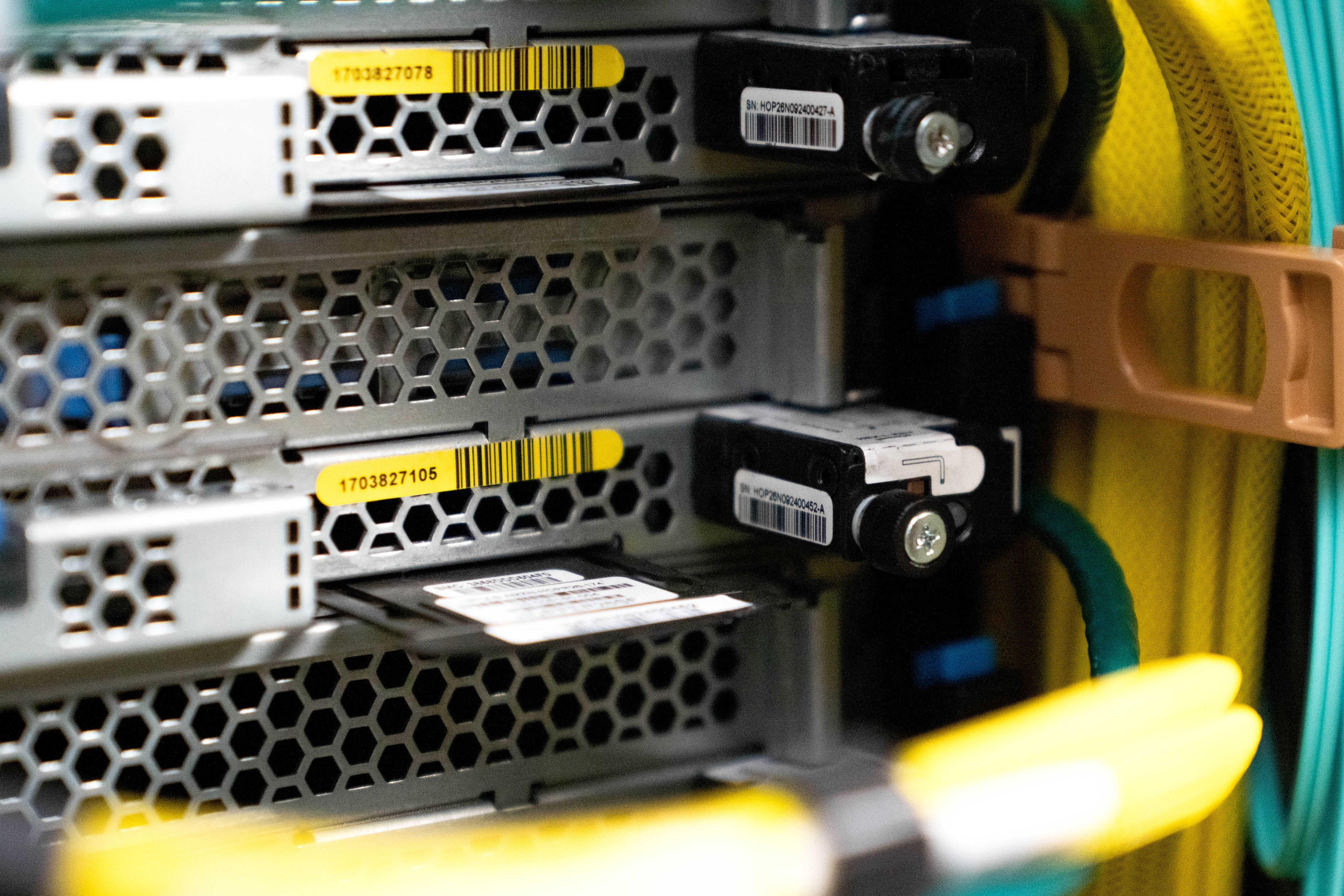 Close-up of server hardware with hexagonal ventilation panels, barcode labels, and colorful cables.