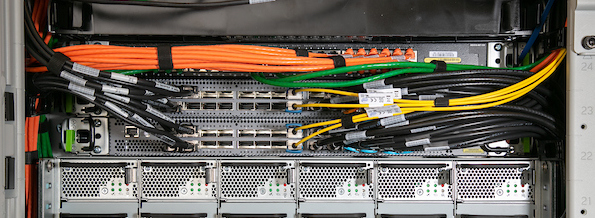Close-up of a server rack with neatly organized orange, green, yellow, and black network cables connected to switches and hardware components.