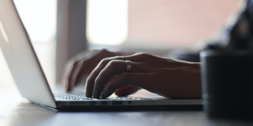 Hands typing on a laptop keyboard in a softly lit room.