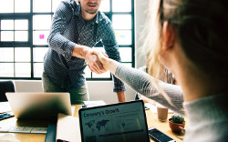 Two people shaking hands in an office setting, with a laptop displaying a "Company's Growth" chart in the foreground.