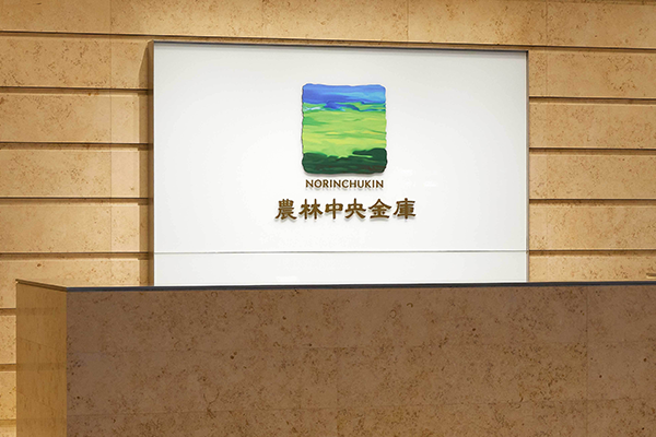 Reception desk at Norinchukin Bank featuring the Norinchukin logo and Japanese company name on a wall sign.