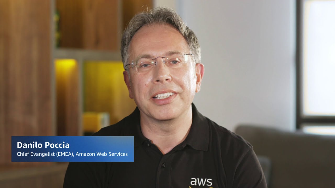 A person wearing an AWS polo shirt is speaking in an indoor professional setting, with a name and title overlay displaying 'Chief Evangelist (EMEA), Amazon Web Services'.