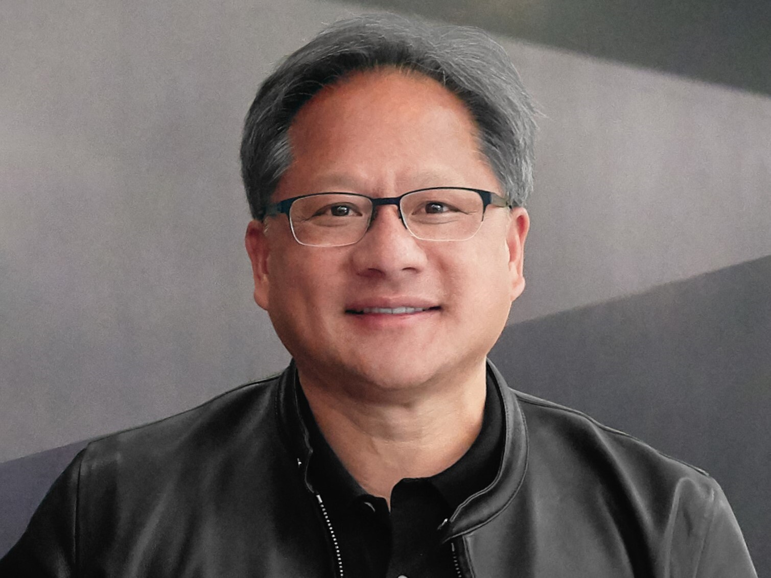 A professional headshot of a person with gray hair, wearing glasses and a black jacket, smiling against a modern blurred background.