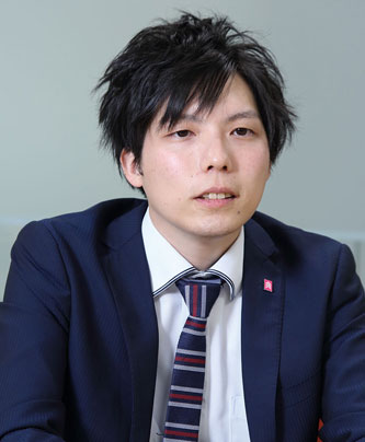 A business professional in a dark suit and striped tie, sitting and facing the camera, with a neutral background.