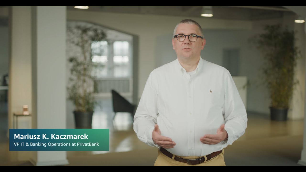 A YouTube video thumbnail showing Mariusz K. Kaczmarek, VP IT & Banking Operations at PrivatBank, standing indoors, wearing a white shirt, and speaking. The background is a modern office environment with plants and soft lighting.