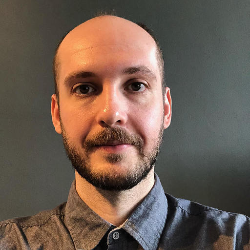 Portrait of a man with a beard in a blue shirt against a plain background