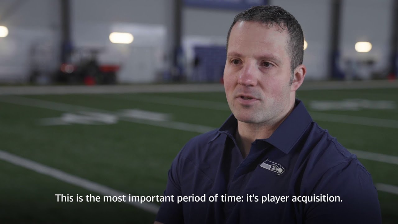 A person wearing a Seattle Seahawks polo shirt is seated in an indoor football field with the caption, "This is the most important period of time: it's player acquisition."
