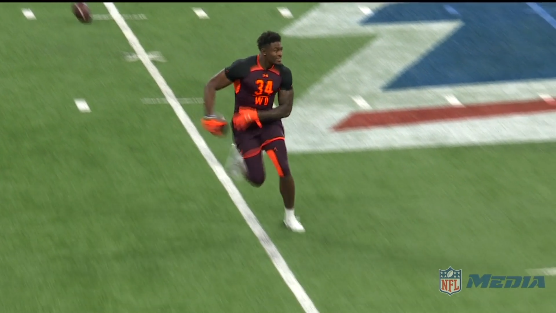 Football player wearing a dark uniform with orange accents running on a field during an NFL event.