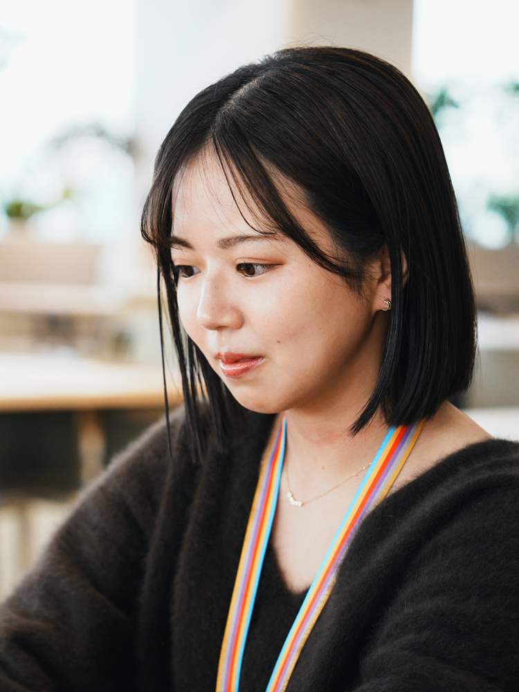 A woman wearing a rainbow lanyard is shown in an office setting, looking focused.