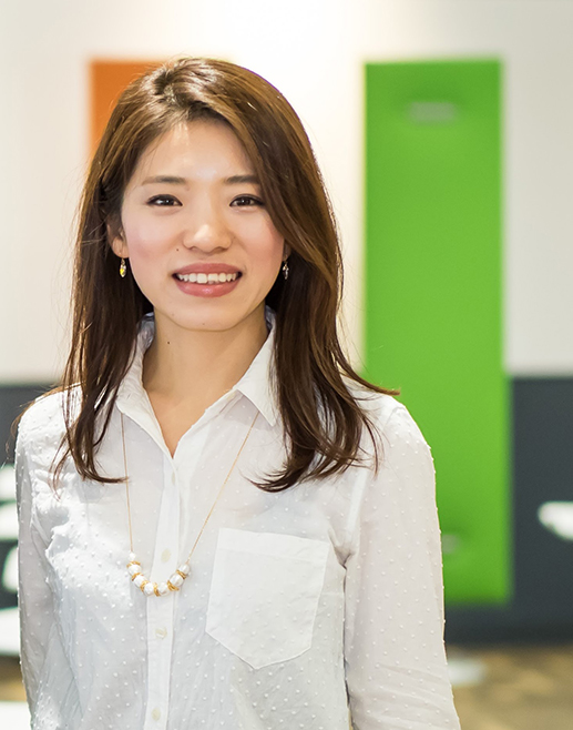 A woman wearing a white blouse standing in an office environment with colorful wall panels in the background.