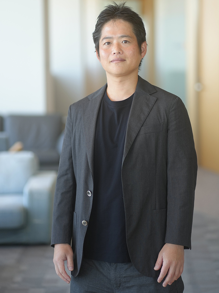 A man in business casual attire stands confidently in a modern office environment.