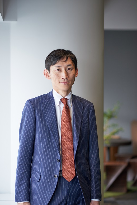 Portrait of a businessman wearing a blue pinstripe suit and an orange tie, standing indoors in a professional setting.