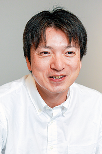 Portrait of a man with short dark hair wearing a white shirt, facing forward and smiling against a plain background.
