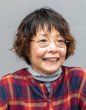 A portrait photo of a smiling person with short hair, glasses, and a red and blue plaid shirt, in front of a neutral background.