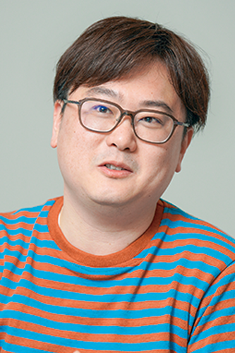 Portrait of a person wearing glasses and a blue and orange striped shirt against a plain background.