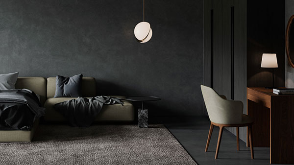 A modern bedroom with dark interior design featuring a minimalist bed, a comfortable armchair at a wooden desk with a lamp, and soft, neutral-toned furnishings and lighting.