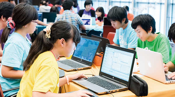 A group of students coding on laptops at a Life is Tech educational camp, collaborating and learning programming skills together.