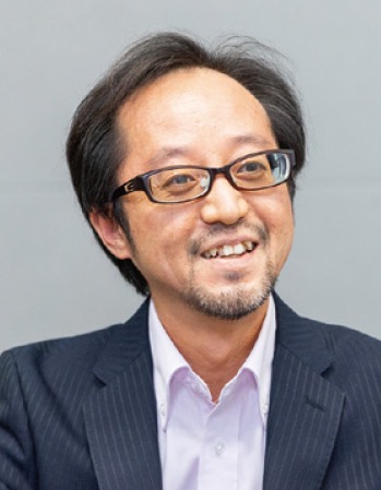 Portrait of a smiling man wearing glasses and a business suit, looking slightly to the side against a plain background.