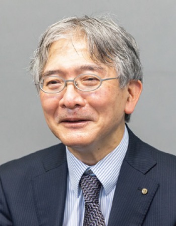 A business executive in a suit, wearing glasses, smiling and looking at the camera against a plain background.