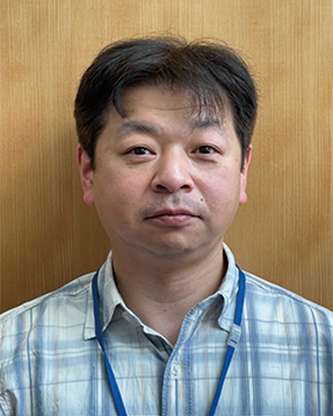 Portrait of a Linkstation employee wearing a plaid shirt and blue lanyard, standing in front of a wooden background.
