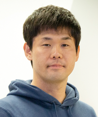 A portrait photo of a man wearing a blue hoodie, facing the camera with a neutral expression, against a light background.