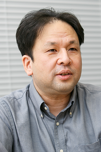 Portrait of an Asahi Kasei employee wearing a gray button-up shirt, photographed in a professional indoor setting.