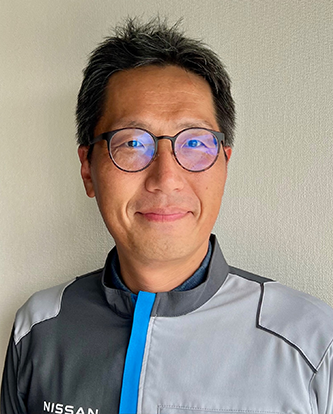 Portrait of a Nissan employee wearing glasses and a Nissan-branded work uniform, standing against a neutral background.