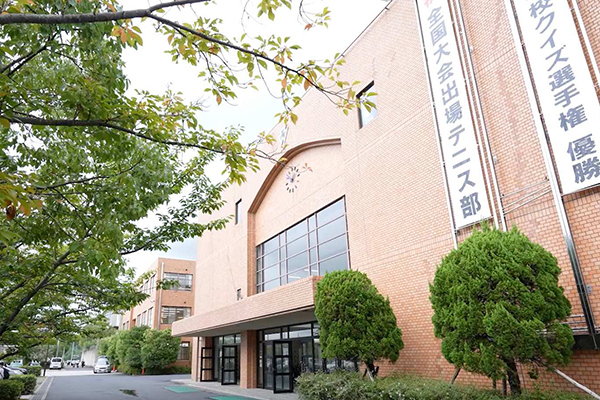 Exterior view of Nishiyamato tennis facility, showing brick building with large windows, entrance, greenery, and Japanese banners on the wall.