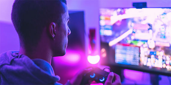 A person playing a video game on a brightly lit screen in a room with purple ambient lighting.