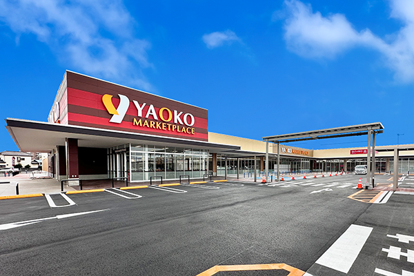 The storefront of Yaoko Marketplace with clear glass windows and prominent signage, set under a bright blue sky.